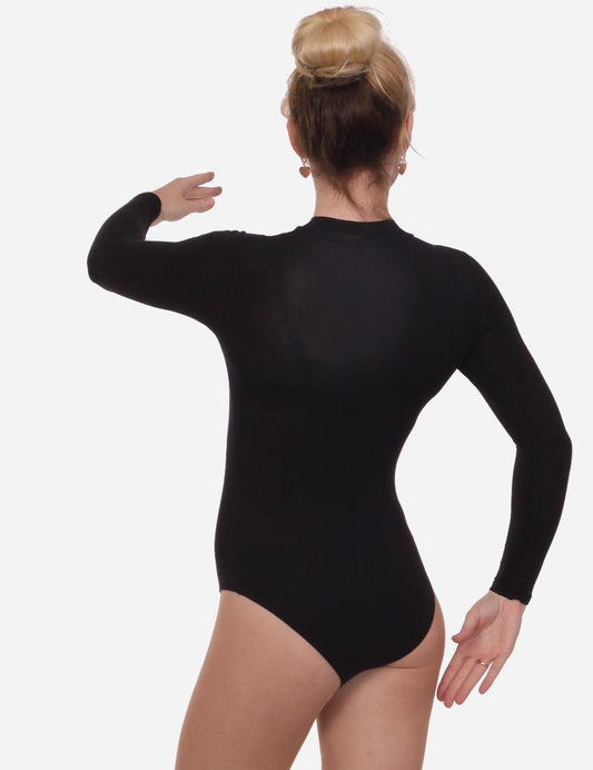Woman in a black mock neck leotard posing with arm extended, bun hairstyle, and black ballet flats on a light backdrop.