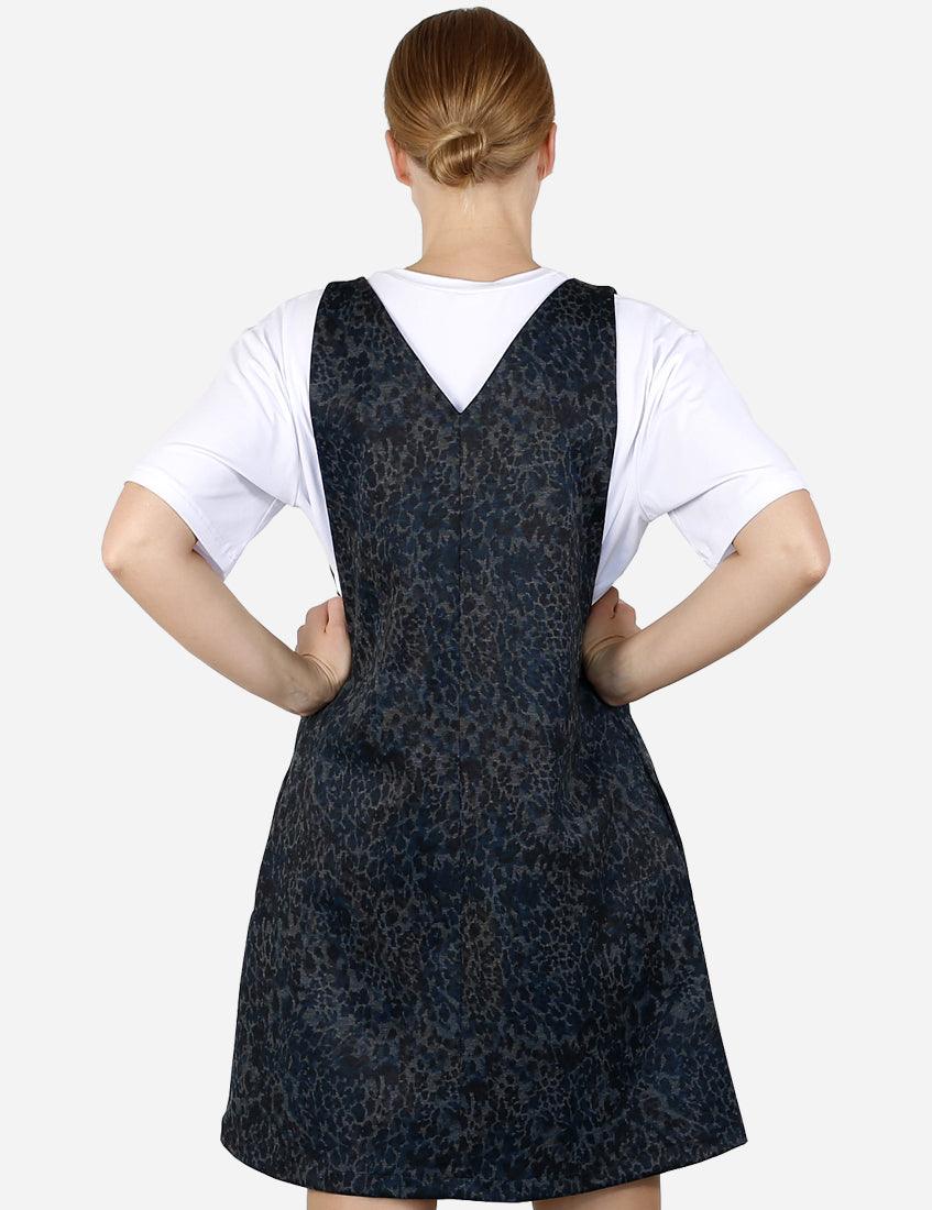Woman from behind wearing a blue patterned pinafore dress over a white t-shirt, looking over her shoulder.