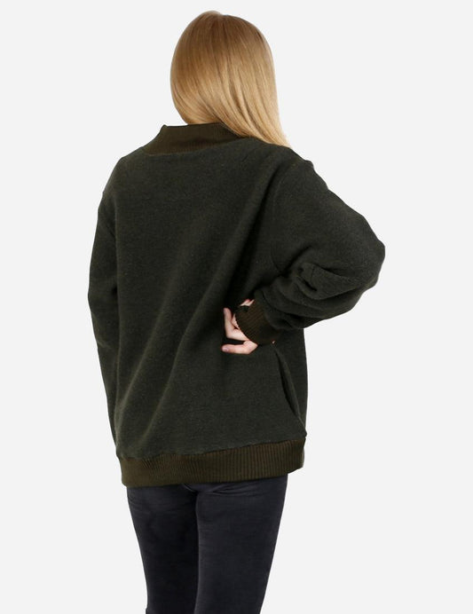 Back view of a young woman showcasing a loose-fitting dark green woolen sweater with a ribbed hem, paired with dark denim.