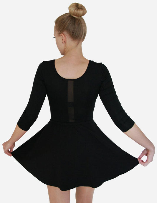 Back view of a woman in a black dress with a large flared skirt, long sleeves, and white ballet flats, isolated on a black background.