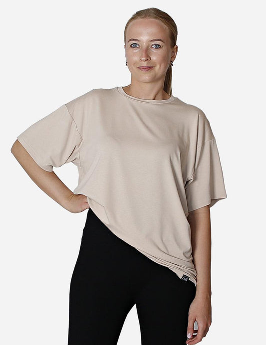 Confident woman in beige oversized unisex t-shirt with black leggings and red sneakers.