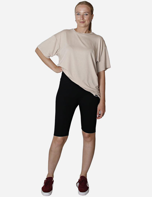Woman showcasing the side view of a beige oversized t-shirt paired with black leggings.