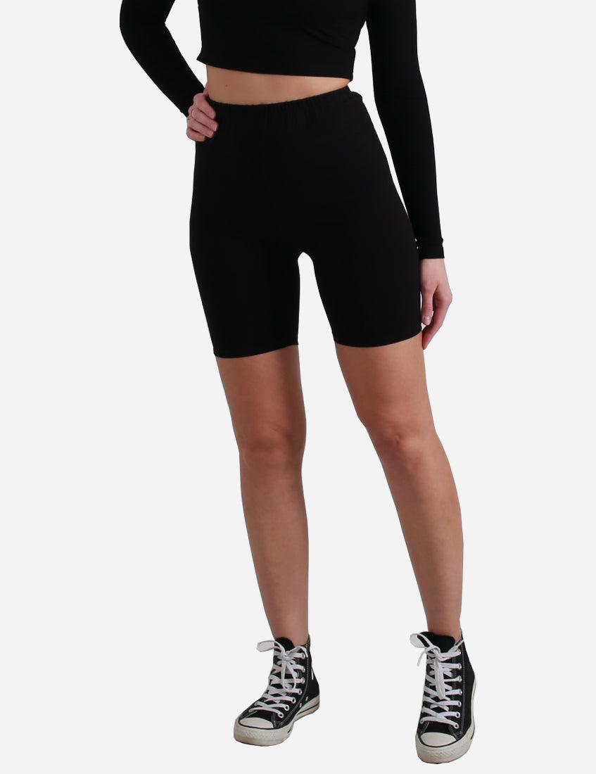 Side view of woman in black cycling shorts and long-sleeve crop top with classic sneakers.