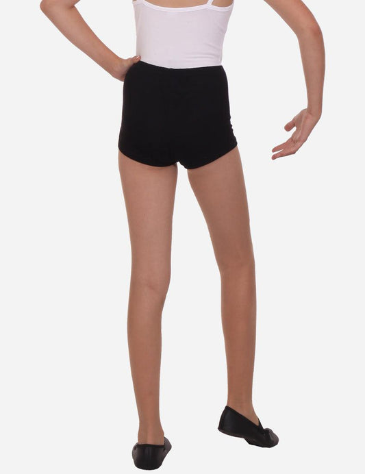 Rear view of black elastic shorts on a young girl, complemented by white ballet flats, against a simple backdrop.
