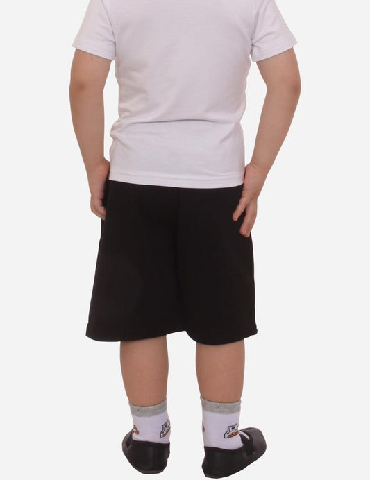 Child in white t-shirt and black shorts standing with hands down, black ballet shoes and white socks, isolated on white background.