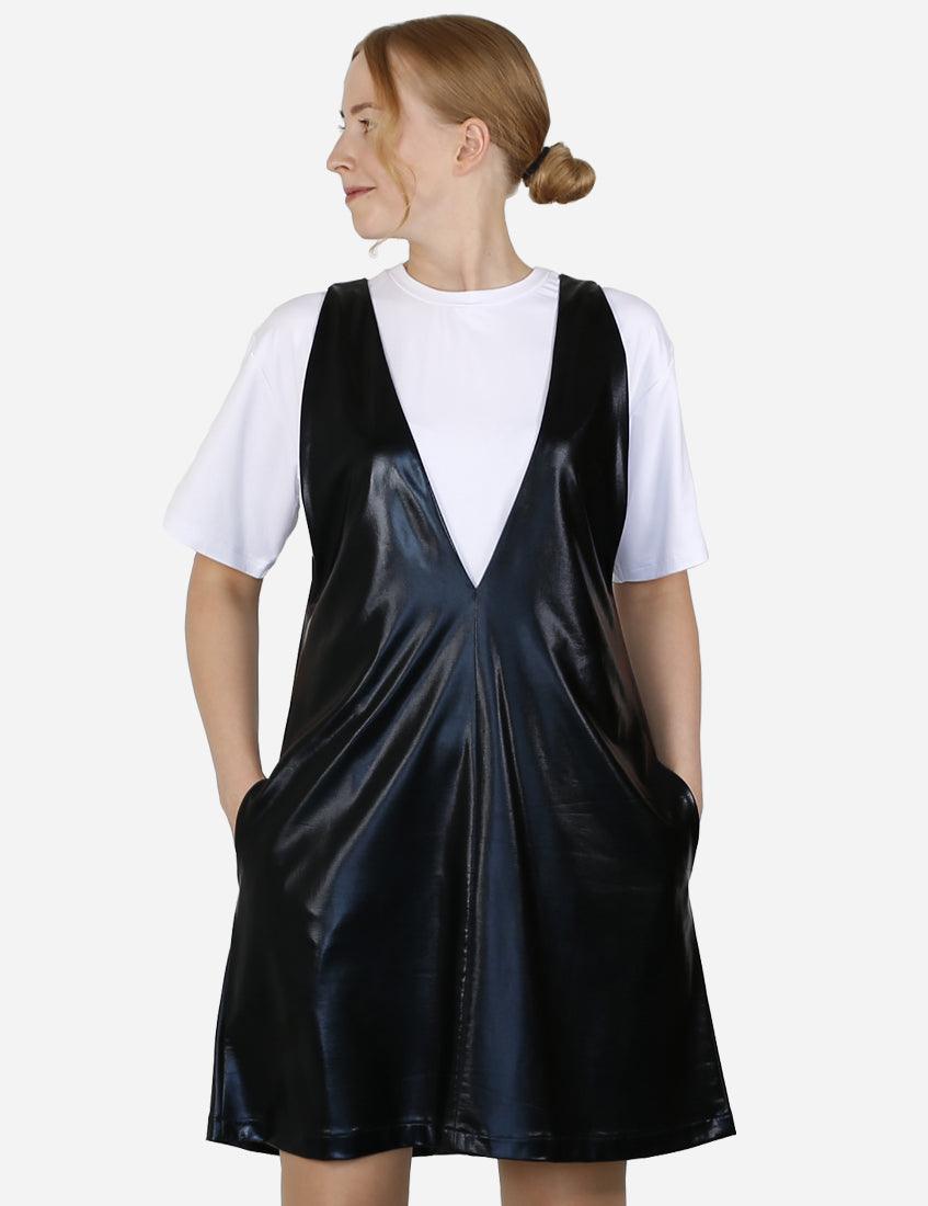 Woman in a contemporary black faux leather pinafore dress over a white t-shirt looking to the side.