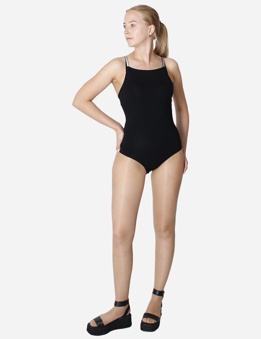 Full body side view of a woman in a black leotard with shiny straps on white background