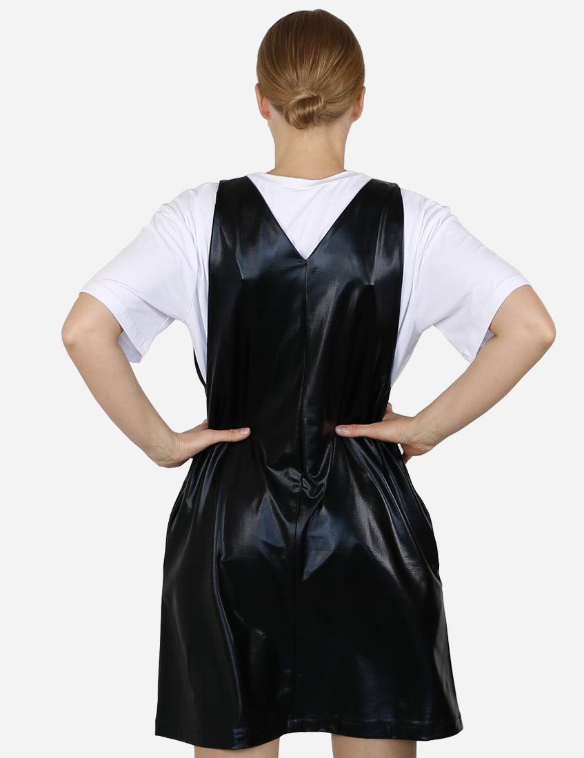 Back view of a woman wearing a modern black faux leather pinafore dress over a white t-shirt.