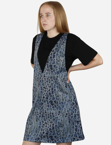 Side view of a woman wearing a blue patterned pinafore dress with a vivid texture over a black tee.