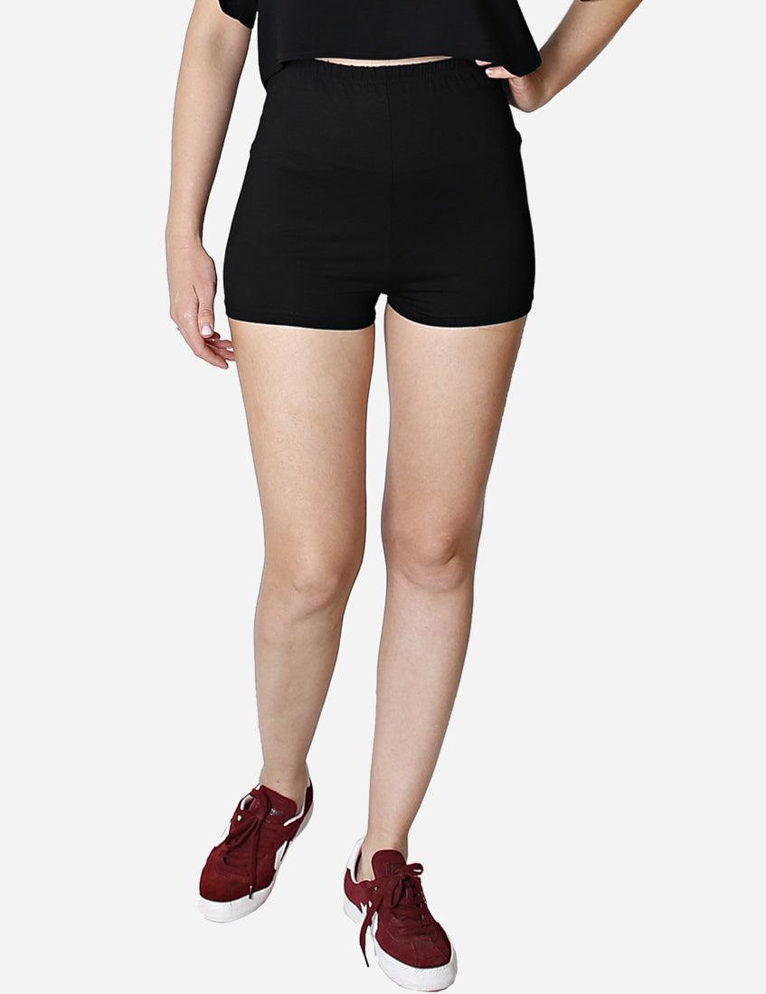 Side view of a woman in high-waisted black shorts and a cropped top, showcasing the profile, with maroon sneakers, isolated on white background.