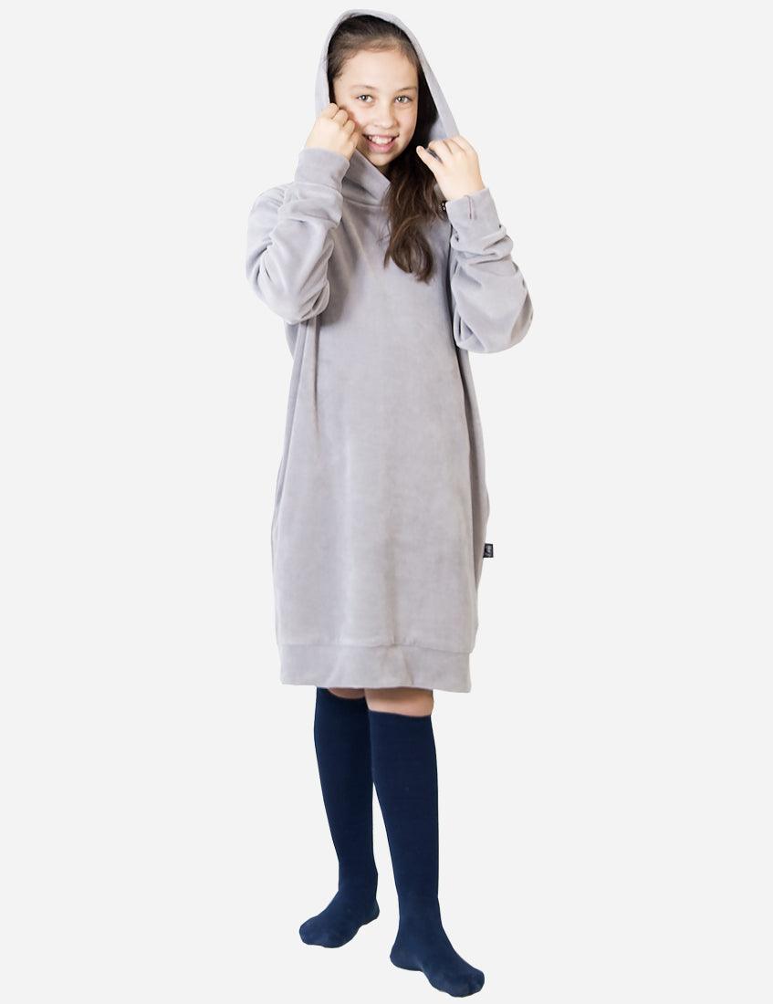Smiling young girl wearing a light grey velvet dress with a hood, paired with navy blue knee-high socks, looking cozy and happy in a casual outfit.