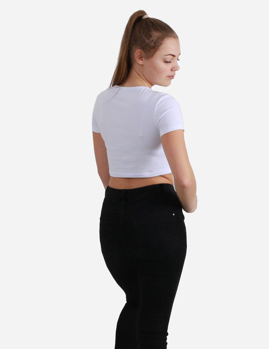 Woman facing away wearing a white short sleeve crop top and black jeans on white background