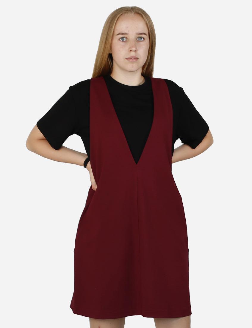 Young woman in a chic burgundy pinafore dress over a black T-shirt, full body shot with beige sneakers, front view.