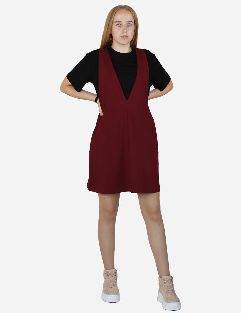 Front view of a young woman modeling a burgundy pinafore dress with a black T-shirt, hands on hips, showing the front cut and fit.