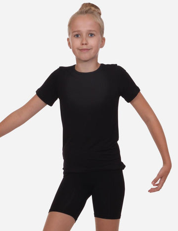 Young girl in a black short-sleeved t-shirt and matching shorts, standing with arms at her sides, isolated on a white background